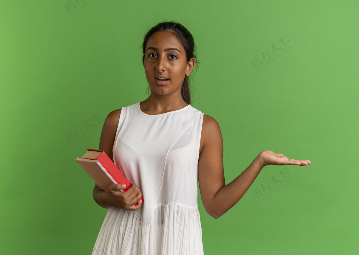 壁板看着镜头 年轻的女学生拿着笔记本 用手指着旁边的书绿色背景年轻