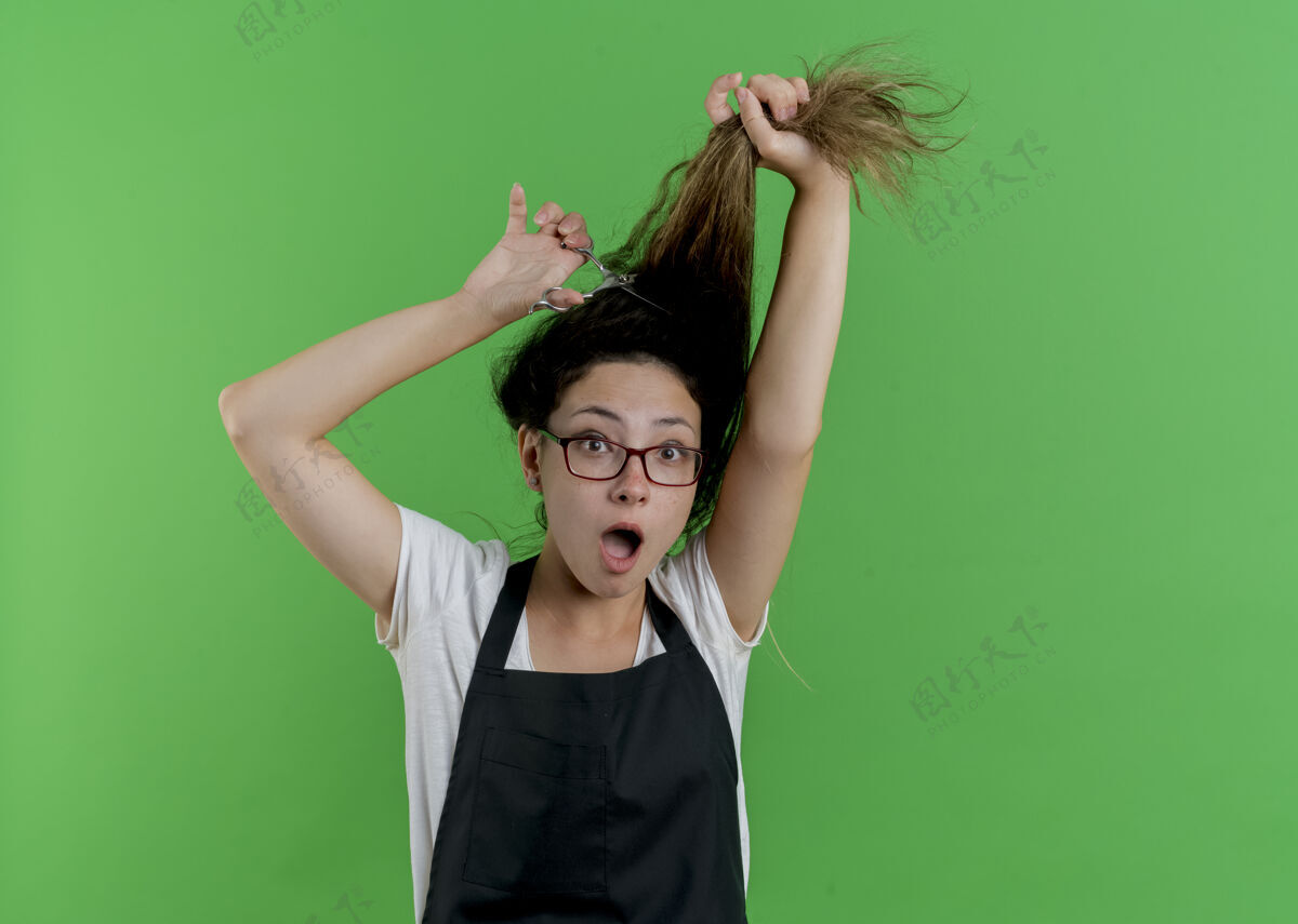 衣服年轻的专业美发师 围着围裙刷洗头发 站在绿色的墙壁上惊讶不已头发站脸