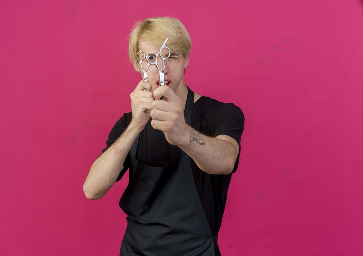 人专业理发师拿着剪刀站在粉红色的墙上看着前面感觉拿着人