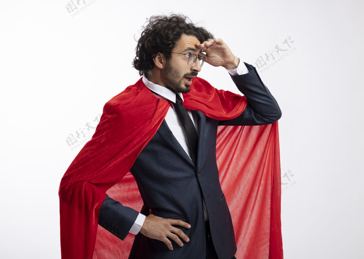 市民惊讶的年轻超级英雄戴着眼镜 穿着红色斗篷的西装 站在一边 手掌放在额头上 看着隔离在白墙上的一边人年轻人侧着