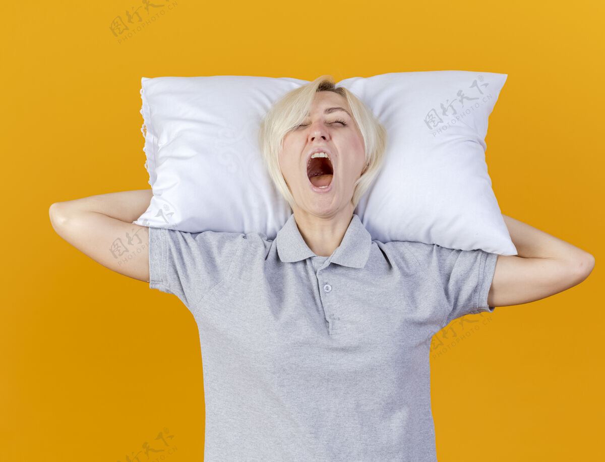 人昏昏欲睡的年轻金发病女人打着哈欠 把头枕在橘色的墙上抱着脸年轻