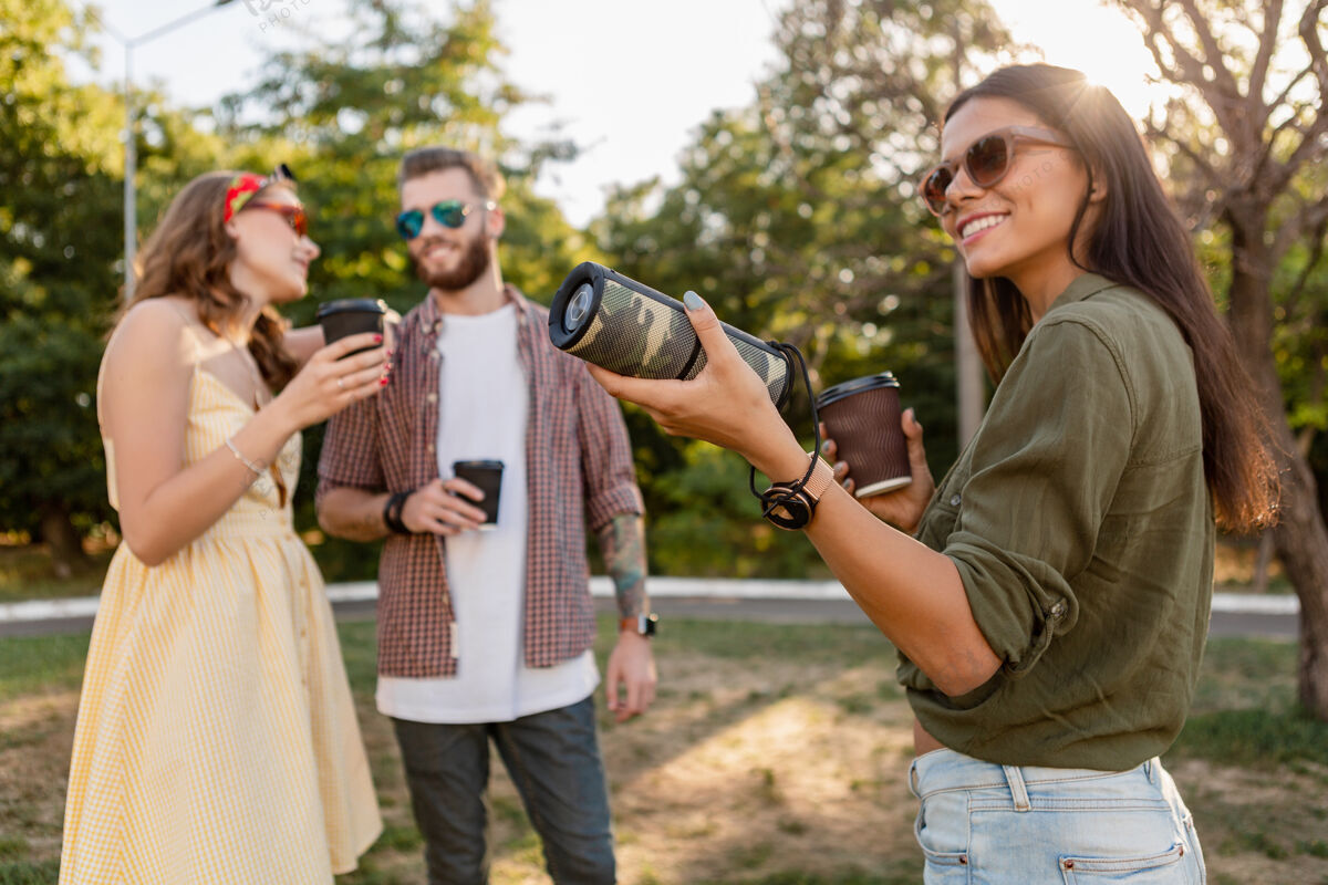 女人年轻时髦的朋友们一起在公园里玩得开心 微笑着用无线扬声器听音乐 夏日风格的季节无线音频音乐