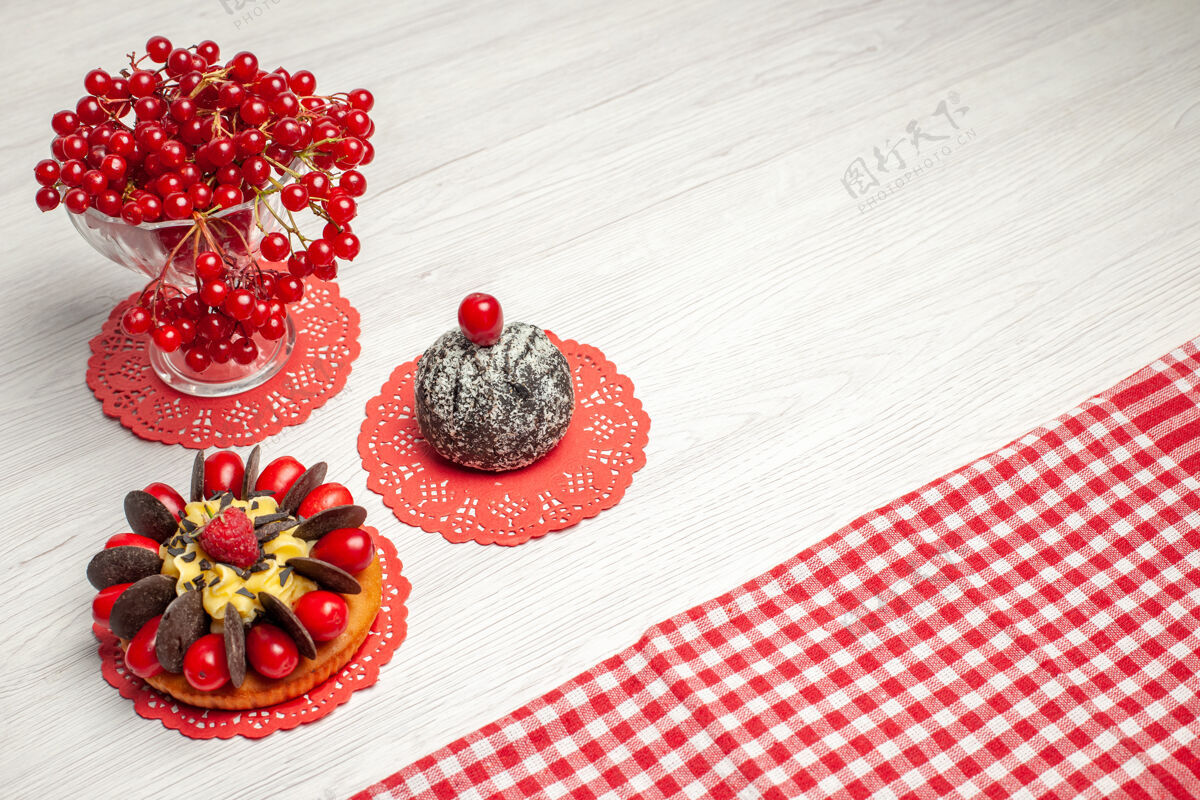 蛋糕上图：红色椭圆形蕾丝桌布上的水晶玻璃浆果蛋糕和可可蛋糕中的红醋栗 白色木桌上的红白格子桌布水晶可可玻璃