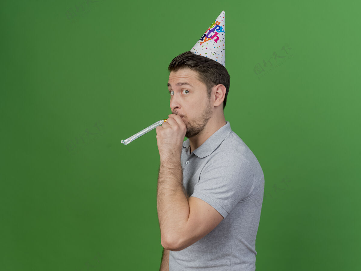吹口哨高兴的年轻人戴着生日帽吹哨子隔离在绿色拜托吹口哨年轻