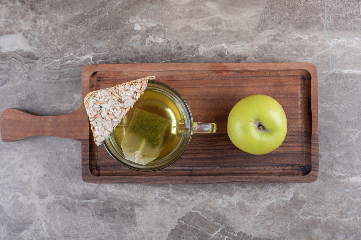 纸板一块膨化的年糕 茶和苹果 在木制托盘上 在大理石背景上美味美味年糕