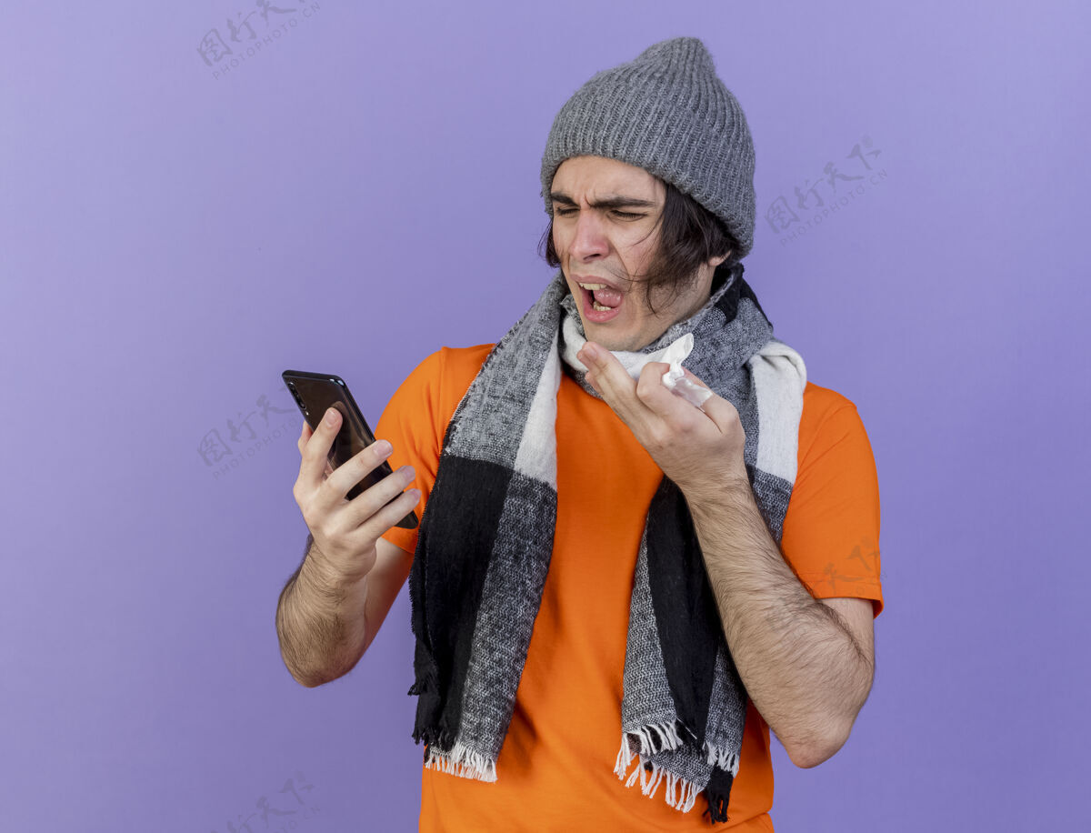 持有愤怒的年轻病夫戴着冬天的帽子拿着围巾 用手指着紫色的电话帽子紫色疾病