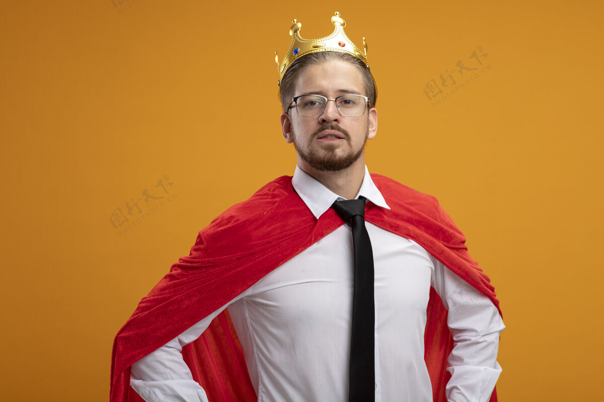 眼镜自信的年轻超级英雄戴着领带戴着皇冠戴着眼镜双手放在臀部橙色隔离领带皇冠手
