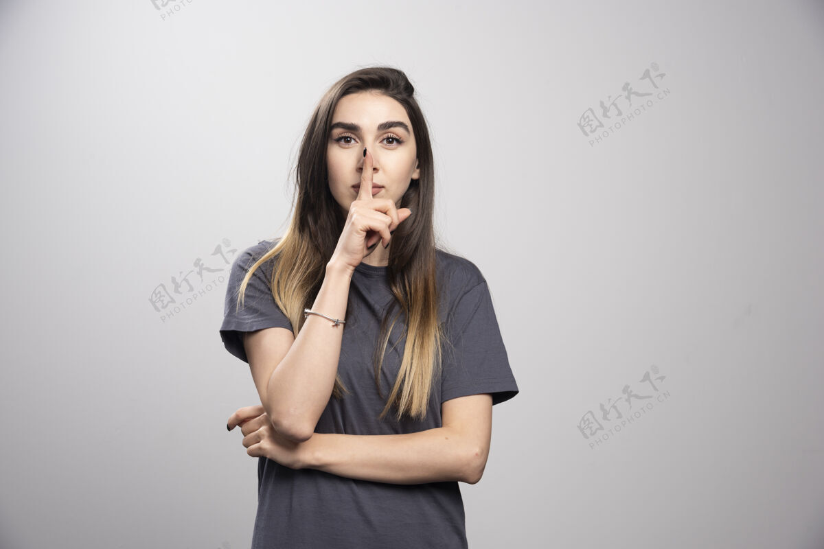 年轻一位年轻女子在灰色背景上做了一个沉默的手势 把手指放进嘴里姿势头情感