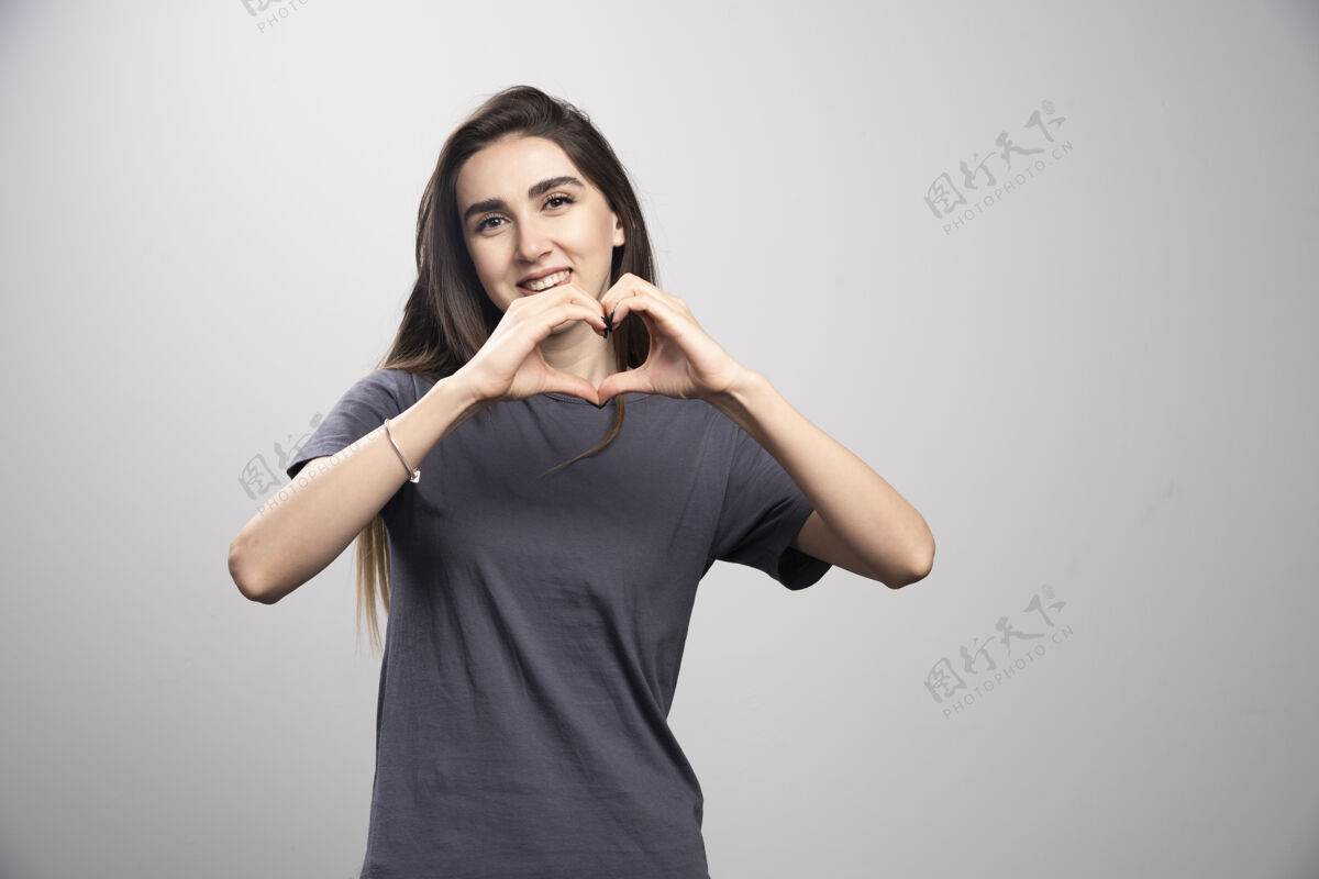 年轻身穿灰色t恤的年轻女子用手在灰色背景上做心形符号姿势女人女人