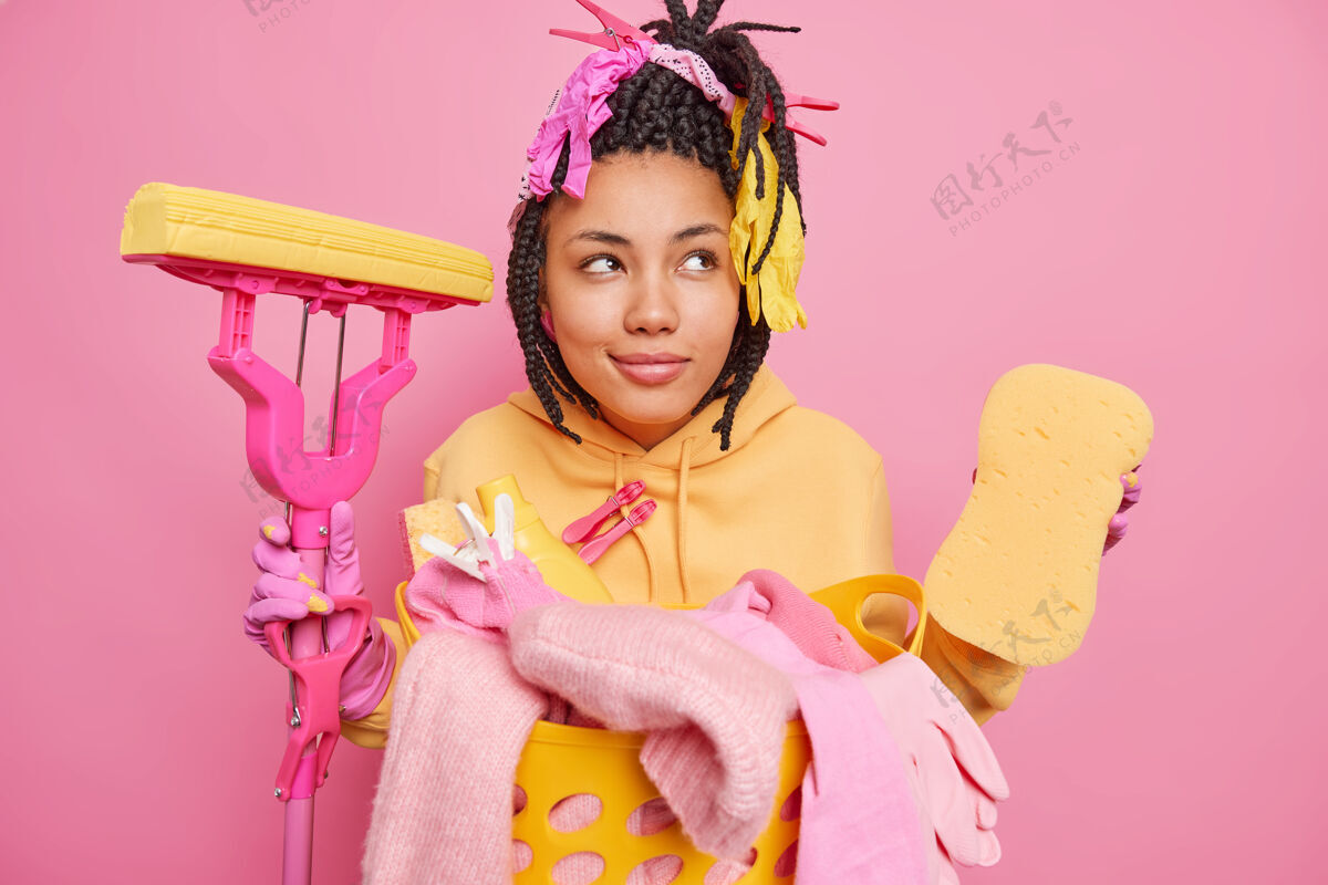 清洁体贴的民族主妇带着沉思的神情 手里拿着干净的工具在粉色的墙上家务成人洗衣