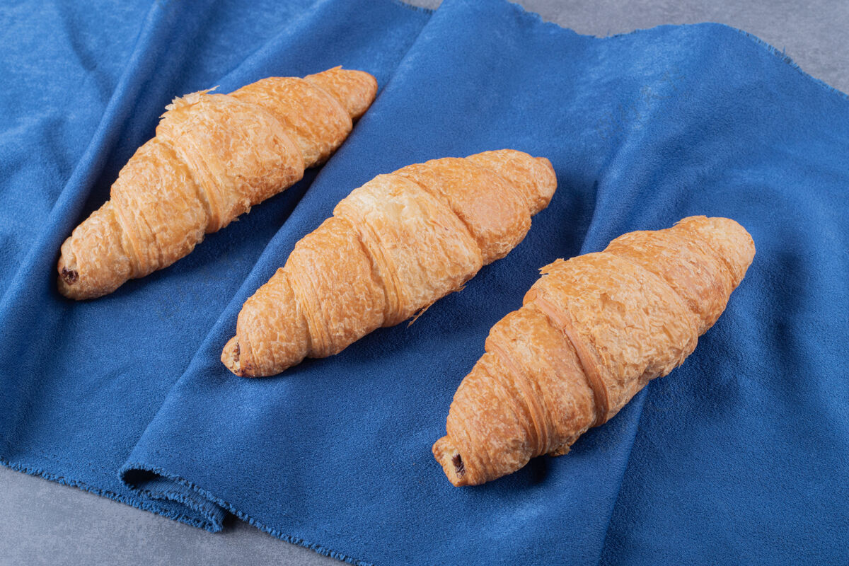 桌子三个新鲜的法式羊角面包放在蓝色餐巾上糕点美食传统