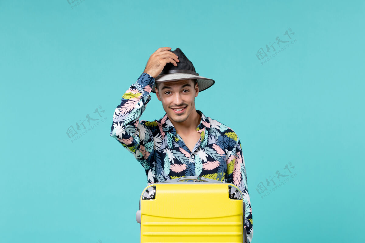 工作前视图的年轻男子与黄色袋举行帽子和准备旅行的蓝色墙壁年轻男性帽子人