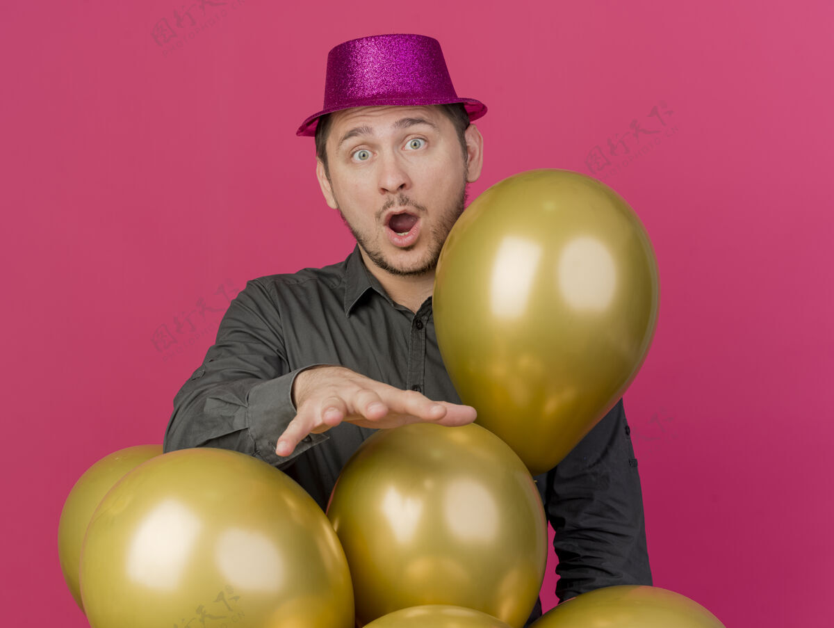 帽子惊讶的年轻人戴着粉红色的帽子站在气球后面孤立的粉红色气球粉色派对