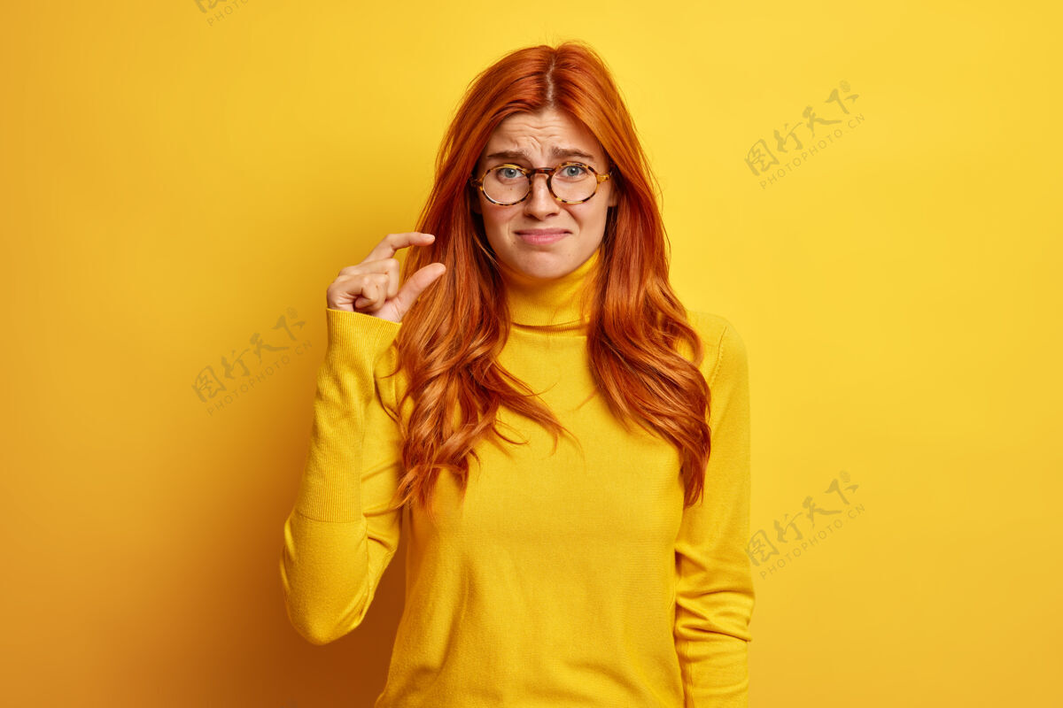 厘米不开心的红发女人做了一个小小的手势 展示了一些穿着休闲套头衫的小东西女性捏数量