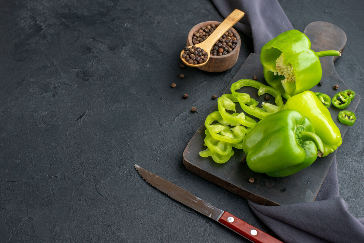 饮食在深色表面的木质砧板上切下的整个切好的青椒的侧视图素食甜椒蔬菜