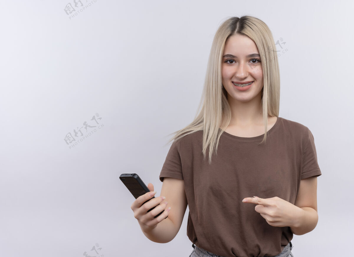 复制微笑着戴着牙套的金发女孩 拿着手机 在一片空白处指着手机 空白处有复印件女孩指向牙科