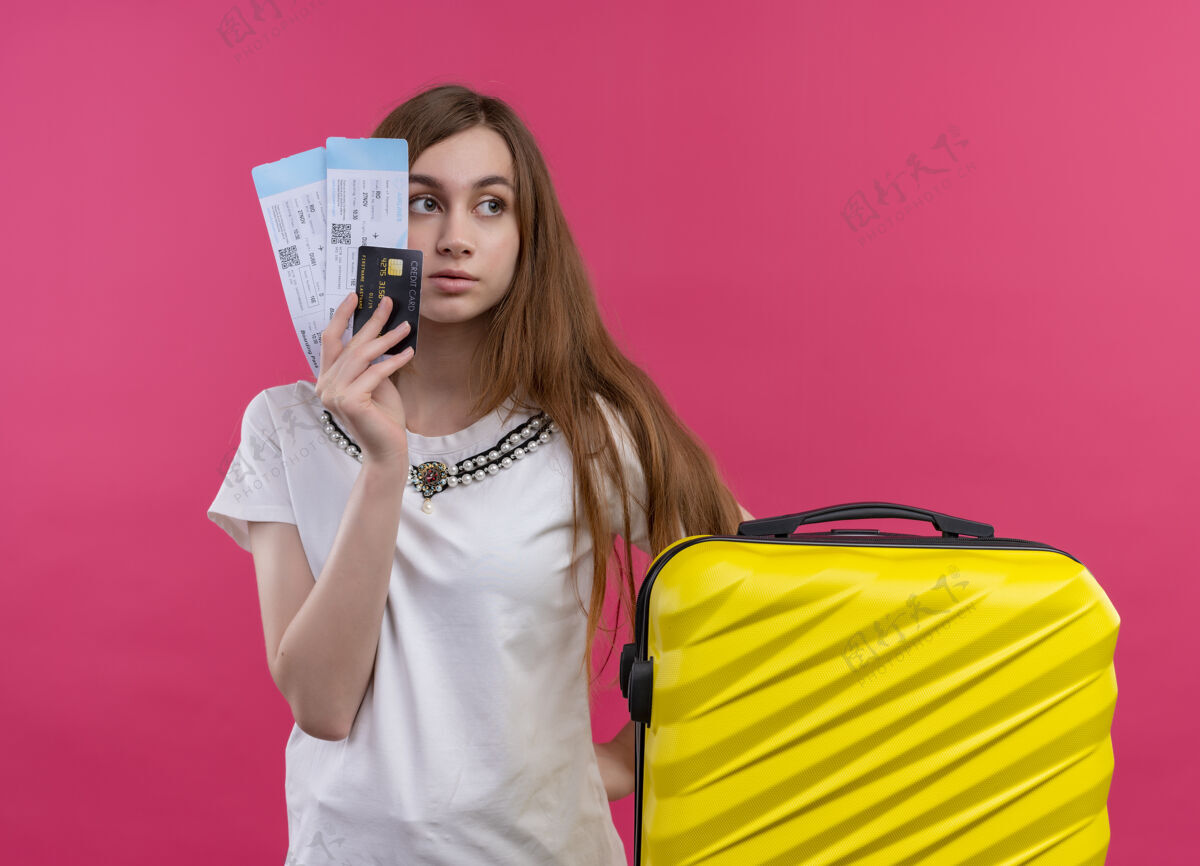 粉红一个神情严肃的年轻旅行女孩手里拿着机票 信用卡和手提箱放在孤立的粉色空间里严重手提箱年轻