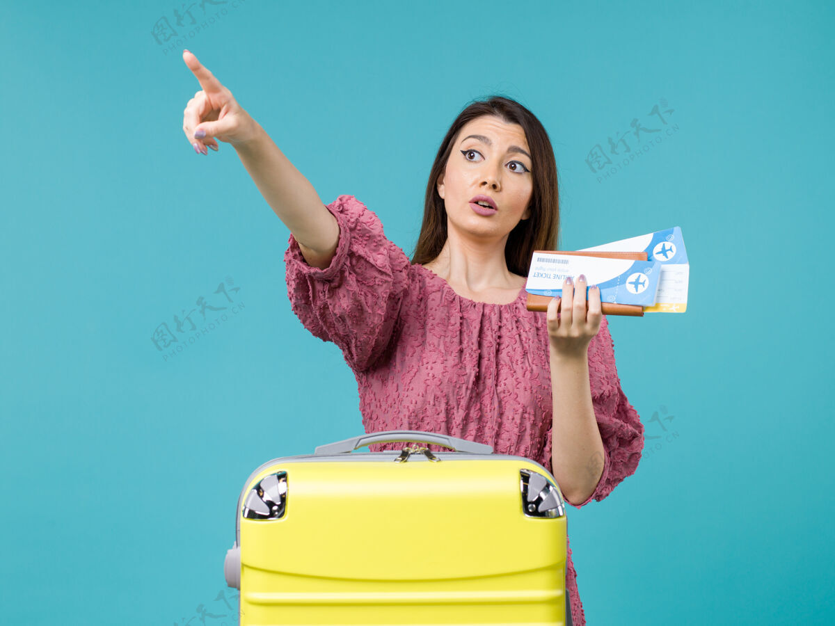 假期正面图度假中的女性拿着钱包和机票指着蓝色背景的某处旅行女性暑假海上旅行旅行前面某处