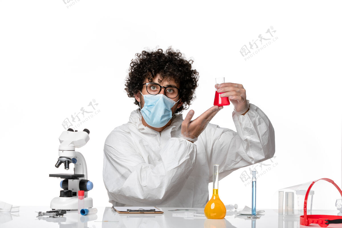 灯光正面图：男医生穿着防护服 戴着口罩 拿着淡白色背景上的红色溶液瓶——流行性冠状病毒外套实验室外套防护