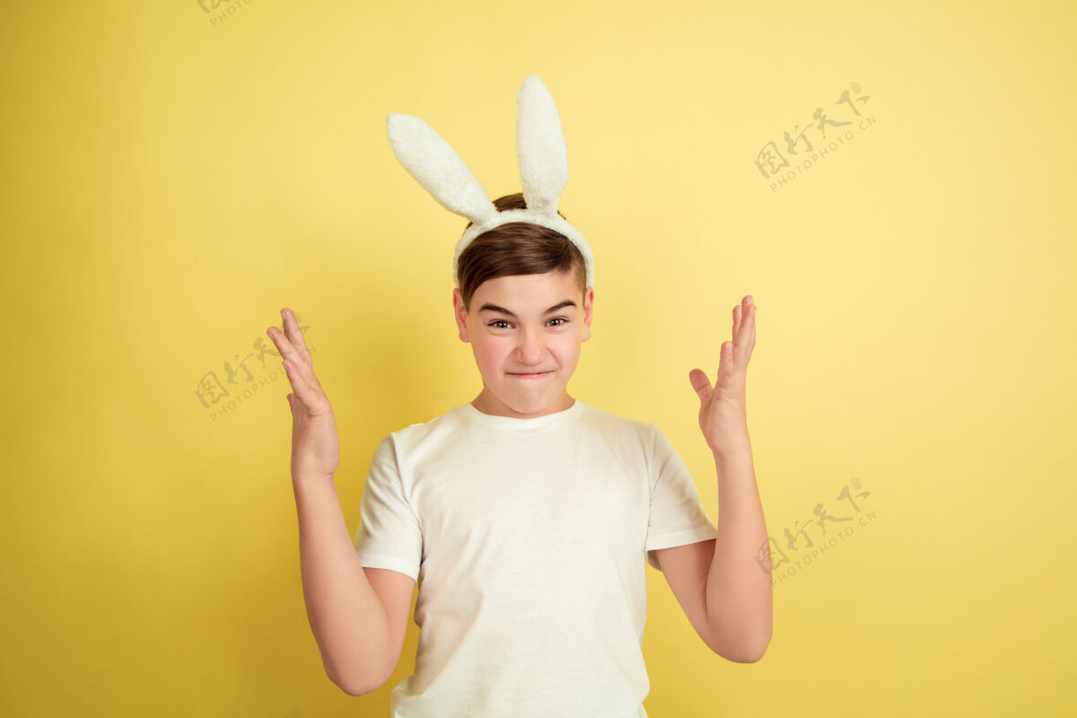 潮流疯狂的指向上白人男孩作为一个复活节兔子在黄色的工作室背景复活节快乐的问候美丽的男模人类情感的概念 面部表情 节日复制空间庆祝面部情感