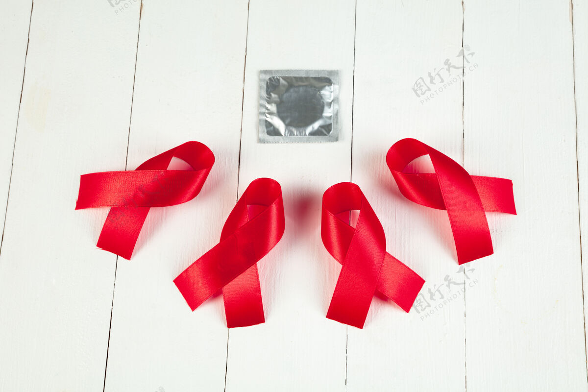 日艾滋病宣传标志红色丝带 白色木桌子背景 带避孕套世界艾滋病日概念健康 帮助 关怀 支持 希望 疾病 保健概念运动世界意识