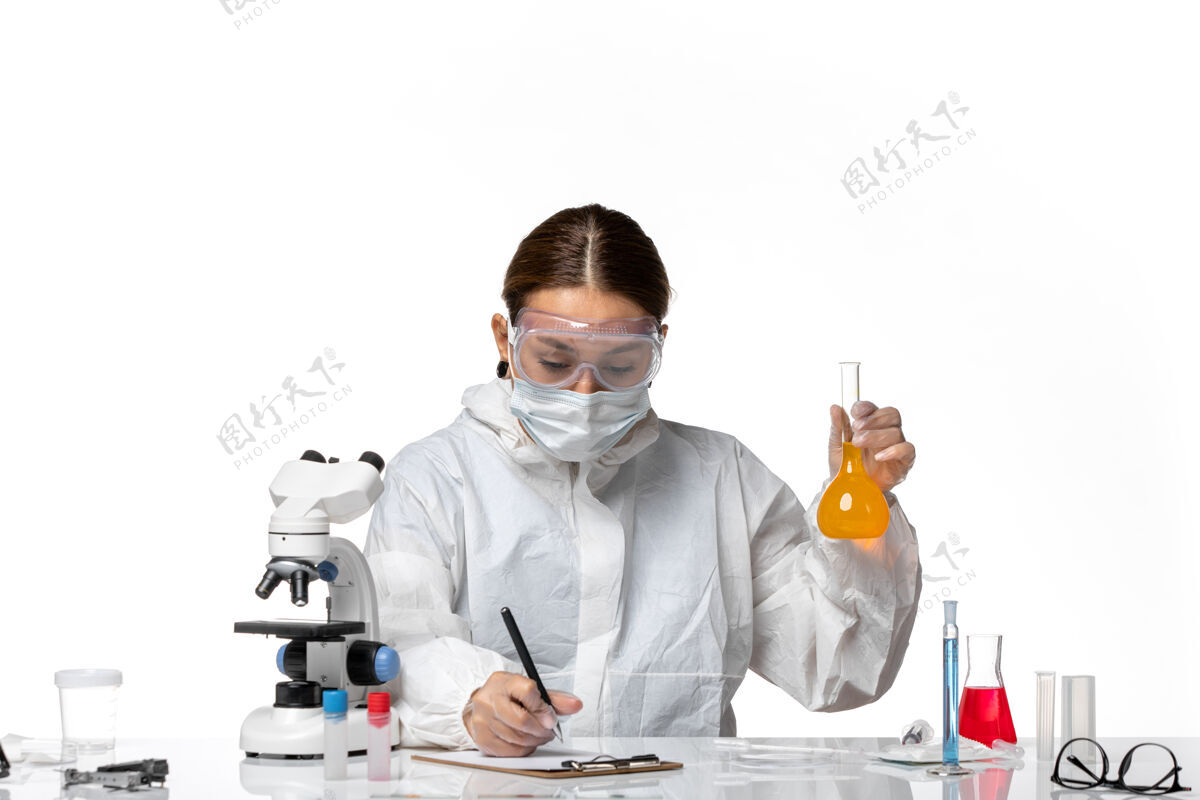 白色正面图女医生穿着特制的工作服 戴着口罩 拿着装有黄色溶液的烧瓶 白色背景上有冠状病毒大流行病毒实验室专业