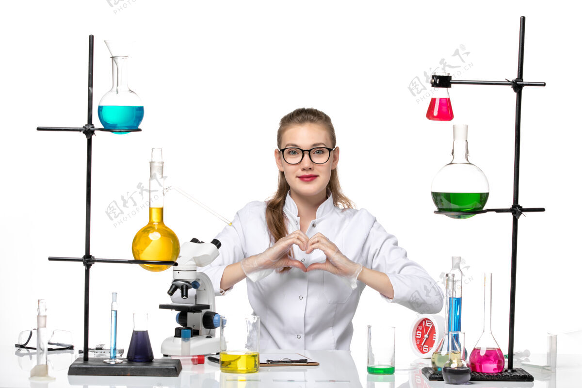 景观前视图身着医疗服的女化学家坐在白色背景化学大流行性冠状病毒上 拿着溶液 展示着爱的标志表演白色人