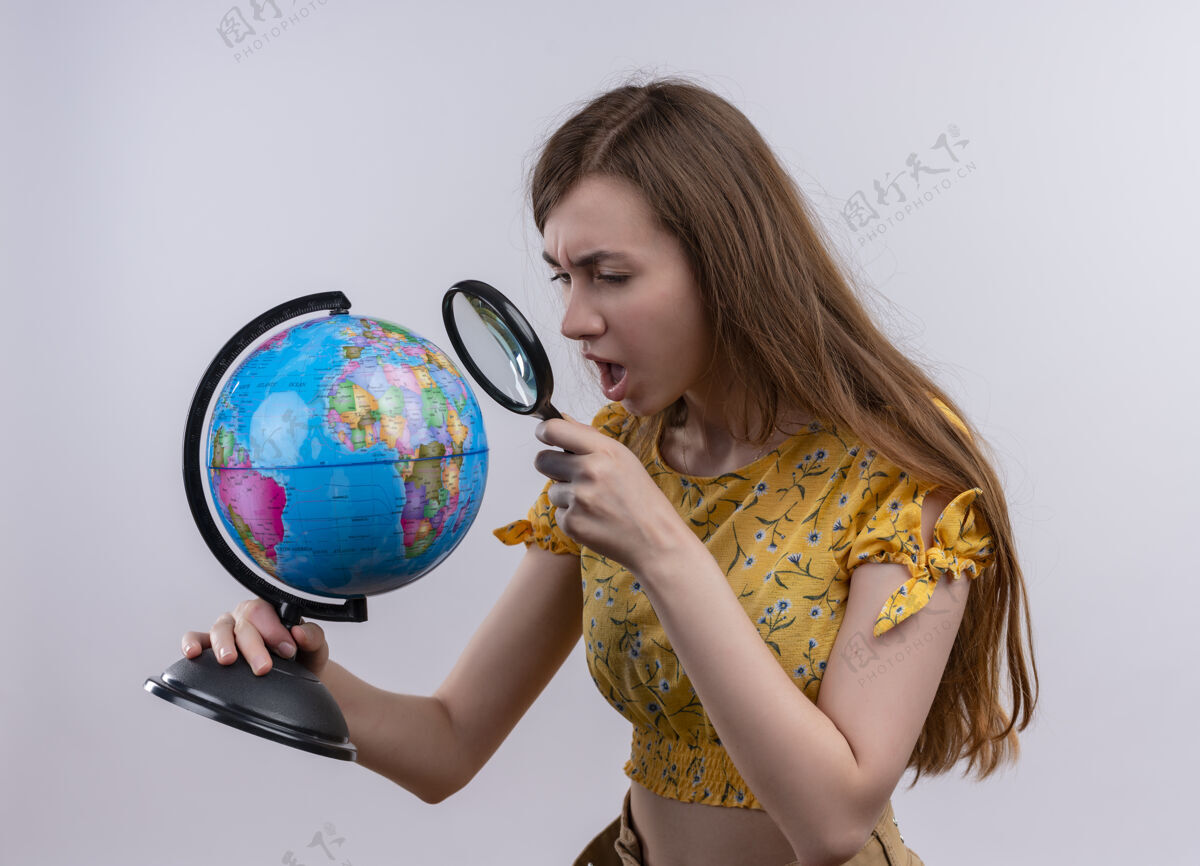 穿过困惑的年轻女孩拿着地球仪 透过放大镜在孤立的白色空间里看年轻女孩放大镜