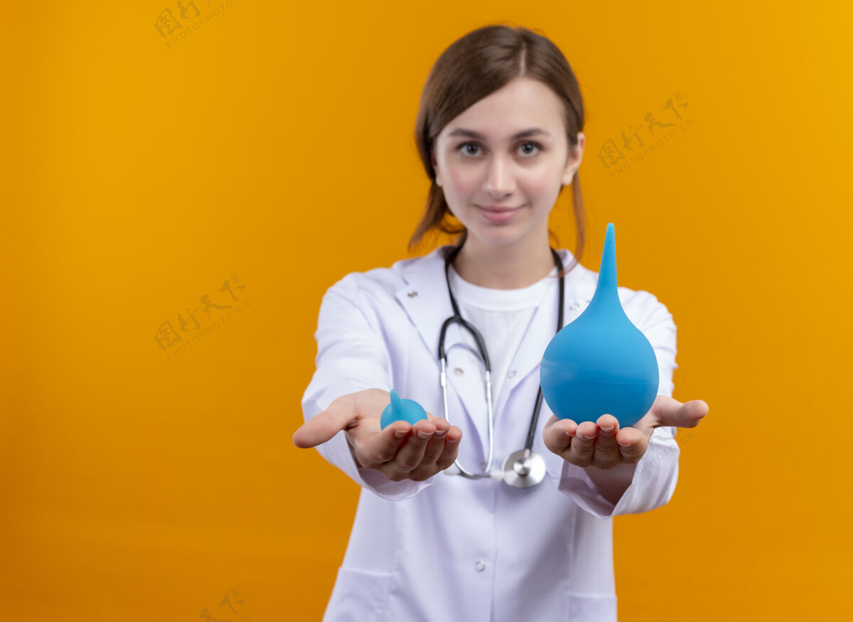 灌肠自信的年轻女医生穿着医用长袍和听诊器 在隔离的橙色空间上伸展灌肠 还有复印空间太空听诊器医生