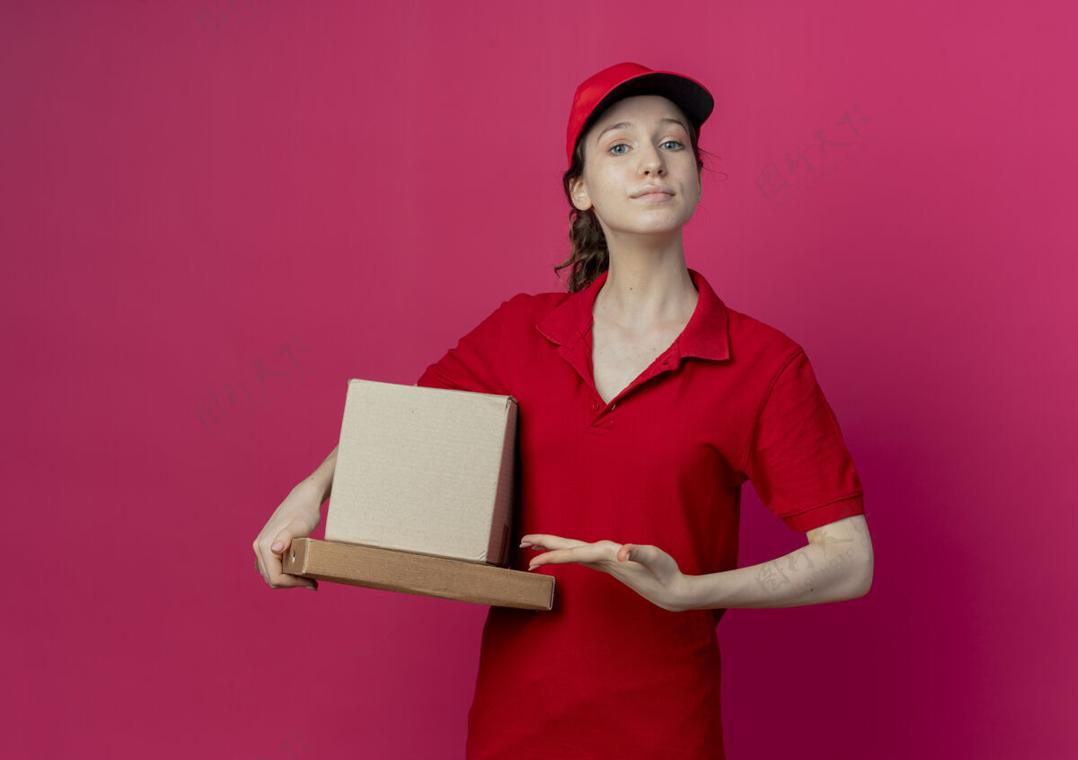 纸箱自信的年轻漂亮的送货女孩 穿着红色制服 戴着帽子 手拿着盒子和披萨 背景是深红色 有复印空间帽子漂亮包装