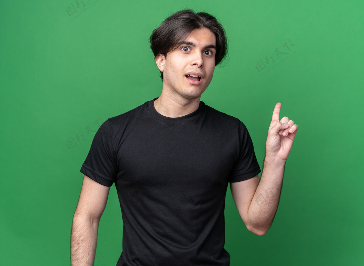 人印象深刻的年轻帅哥穿着黑色t恤点在后面 隔离在绿色的墙壁与复制空间衣服印象站