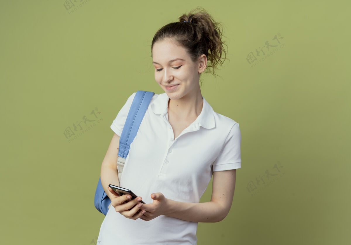 漂亮很高兴年轻漂亮的女学生背着书包拿着手机 看着绿色背景上的空白复制品包电话请