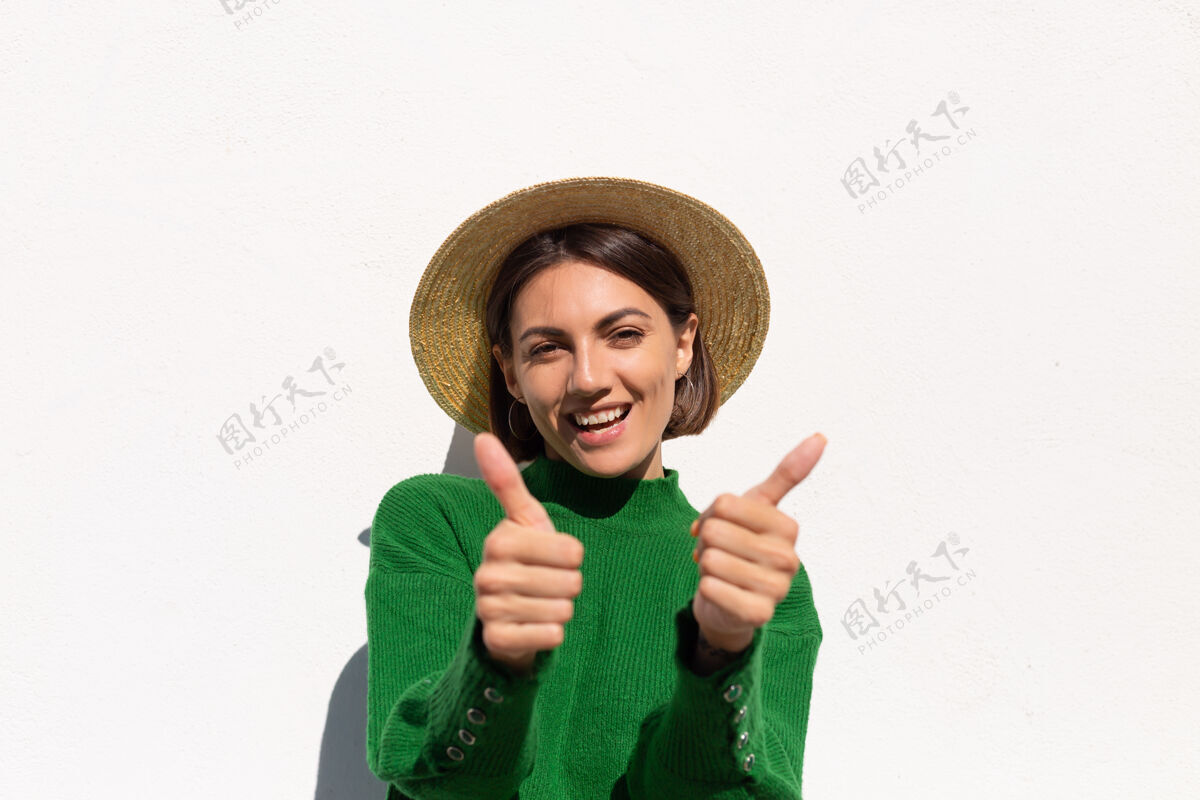 快乐穿着绿色休闲毛衣和帽子的时髦女人在户外白墙上欢快 快乐 兴奋地享受炎炎夏日肖像梦想无忧无虑