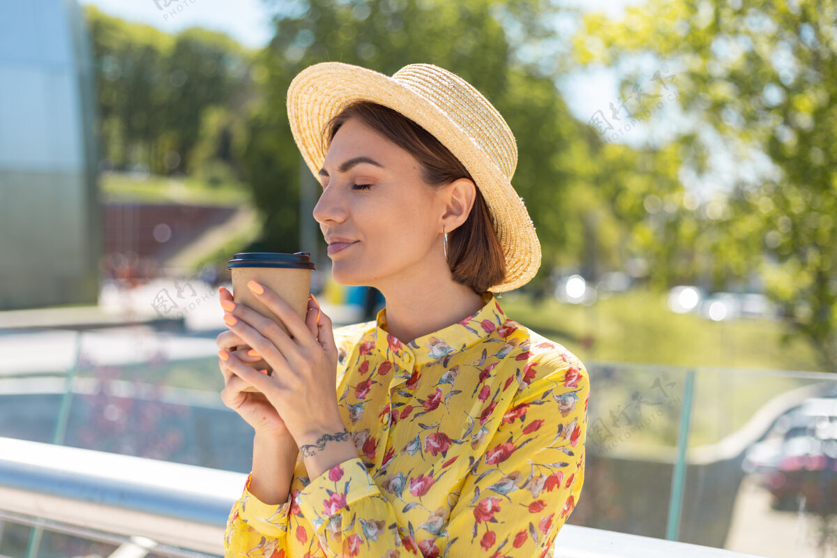 户外穿着黄色夏装 戴着帽子 喝着咖啡 享受阳光的女人的户外肖像女人芳香度假