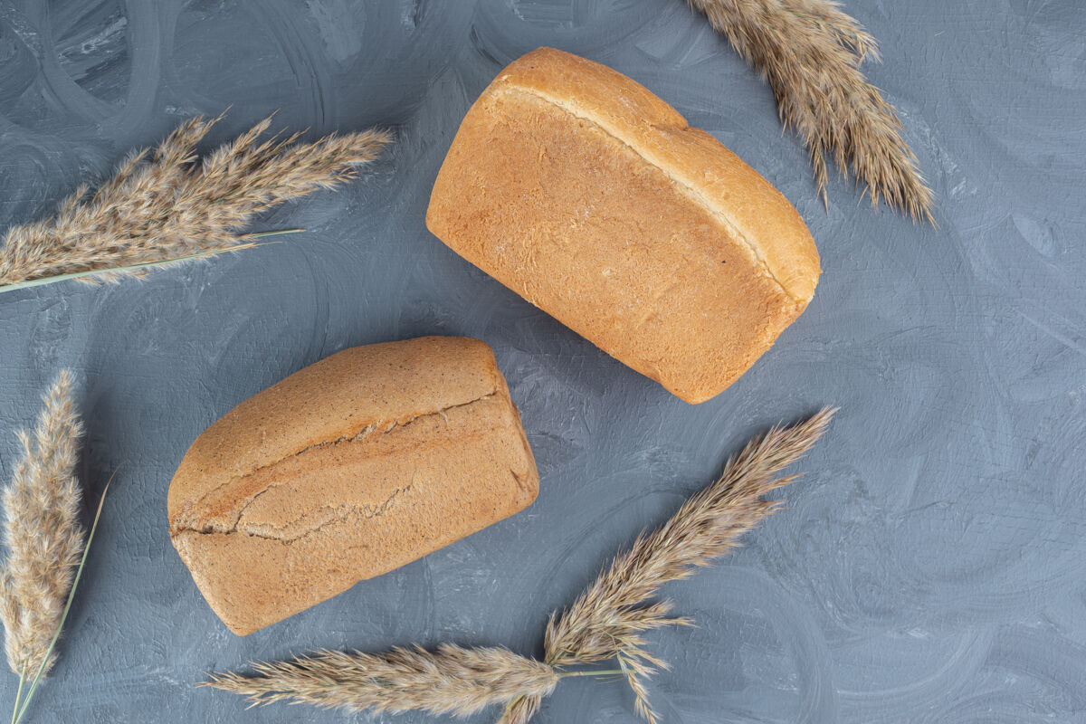 面粉大理石桌上摆着两个面包 面包周围是干羽毛草茎羽毛草美味烘焙