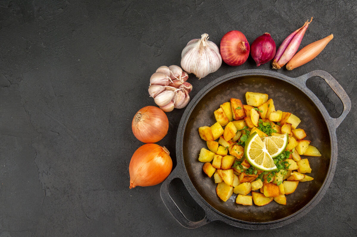 可食用水果俯视图美味的煎炸土豆内锅与柠檬和大蒜周围的黑暗表面水果美食里面