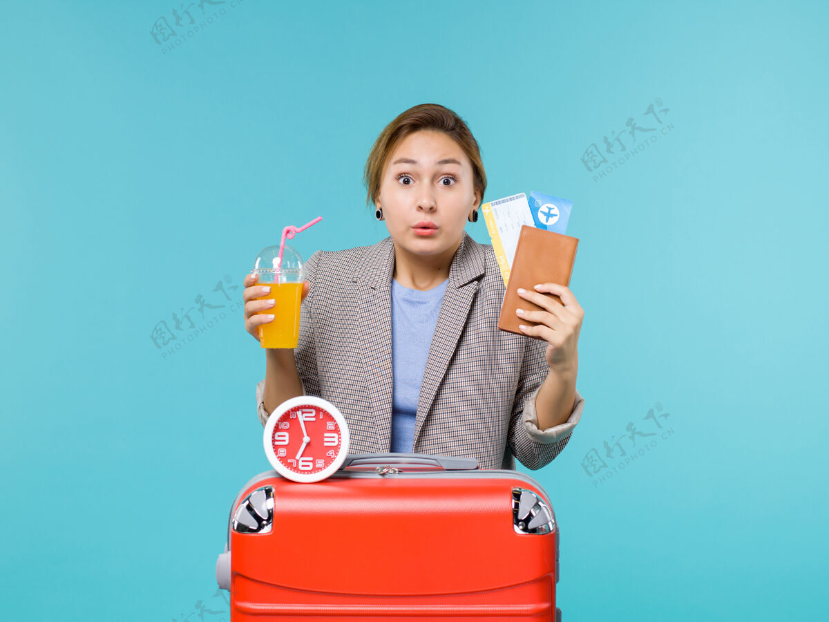 果汁正面图：度假中的女性手持机票和新鲜果汁 在蓝色背景下远航出海度假人微笑举行