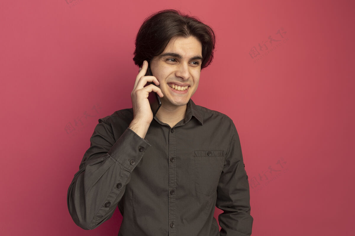 感觉笑眯眯地看着身边穿着黑色t恤的年轻帅哥在电话里说话 隔离在粉红色的墙上微笑站着穿着