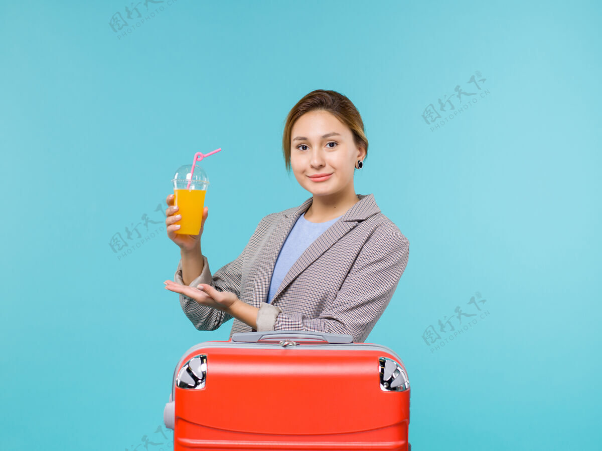 果汁前视图女性在度假与她的红色袋子举行的蓝色背景度假飞机旅行海上旅行新鲜果汁微笑旅行前面