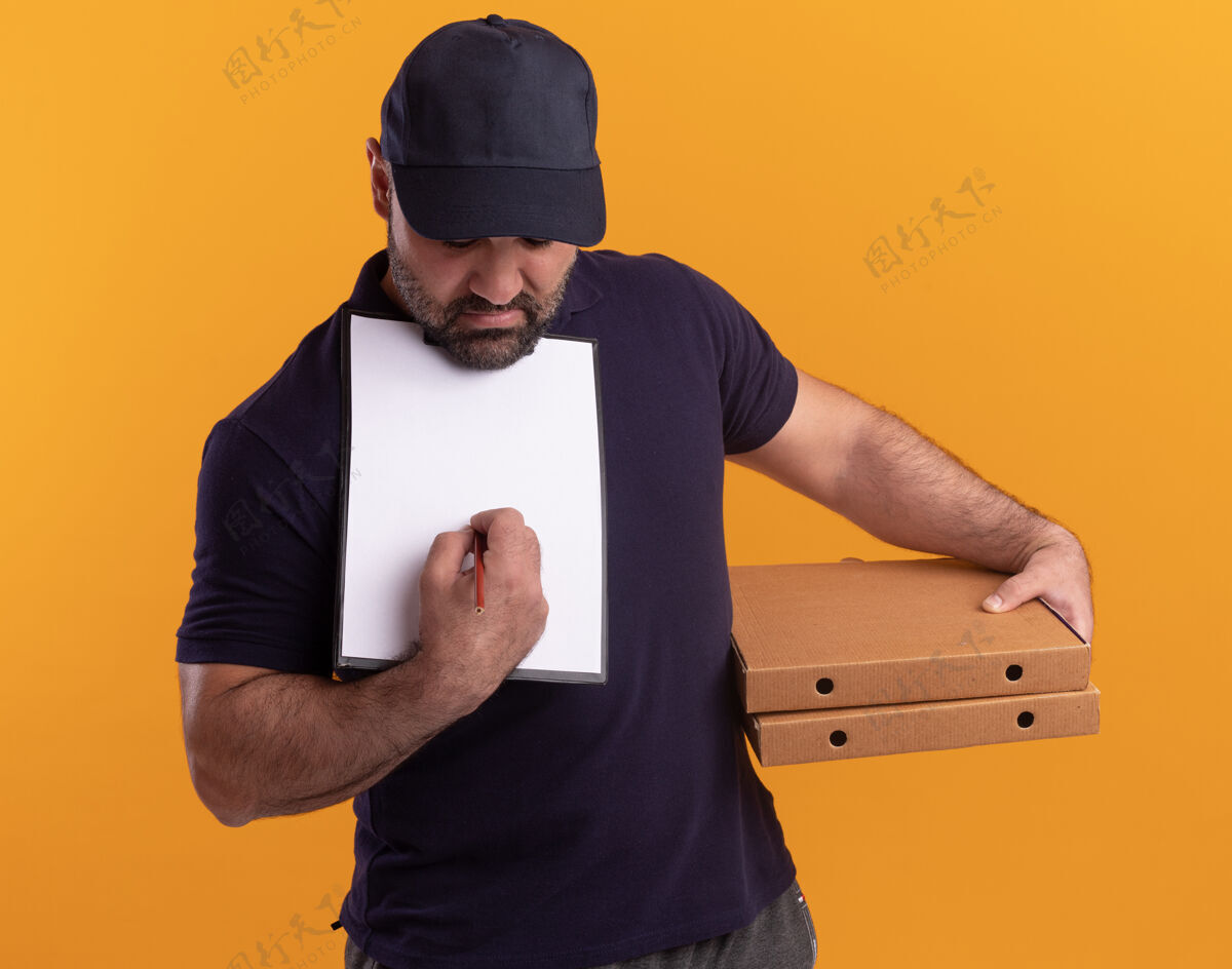 脸一个穿着制服 戴着帽子的中年送货员拿着披萨盒 在黄色墙上的剪贴板上写着什么盒子人拿着