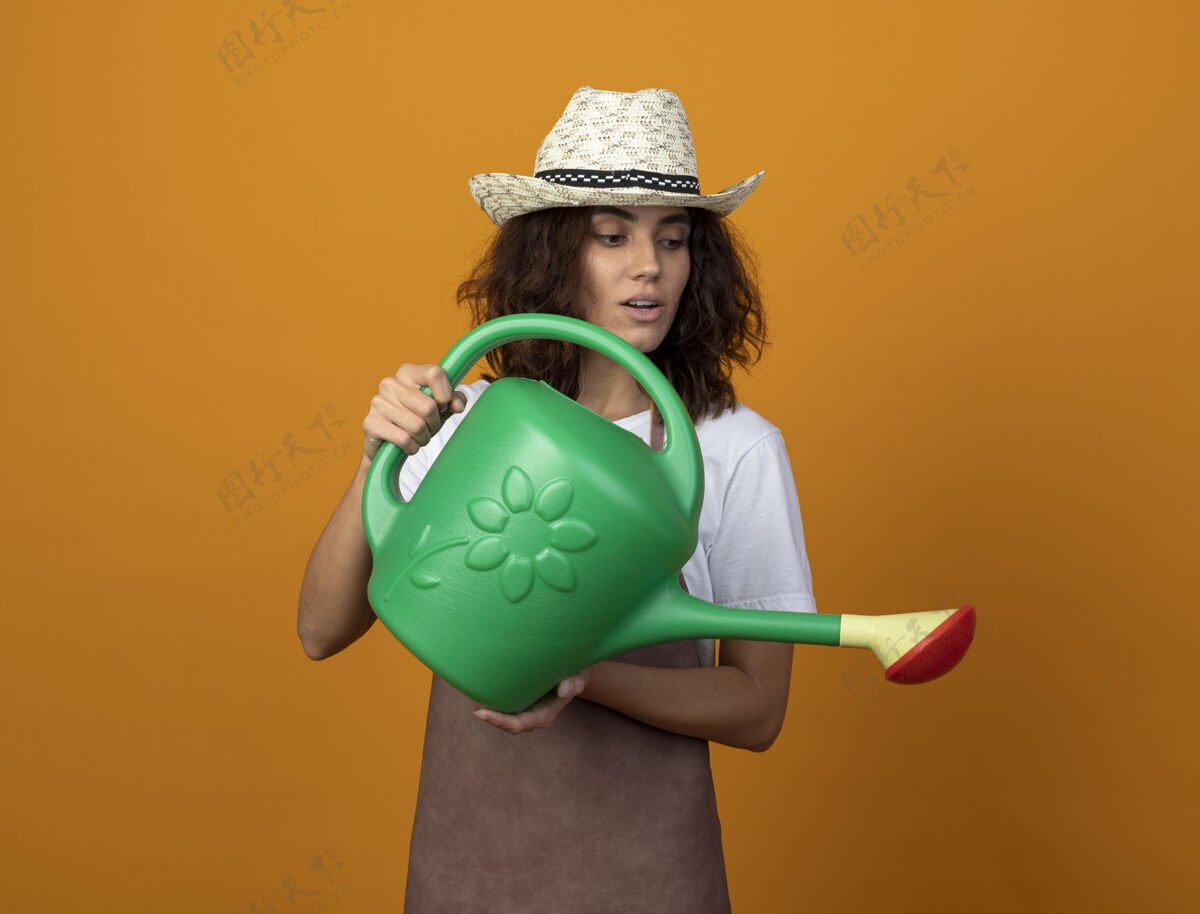 穿穿着制服的年轻女园丁高兴地戴着园艺帽 用水壶浇水浇水制服年轻