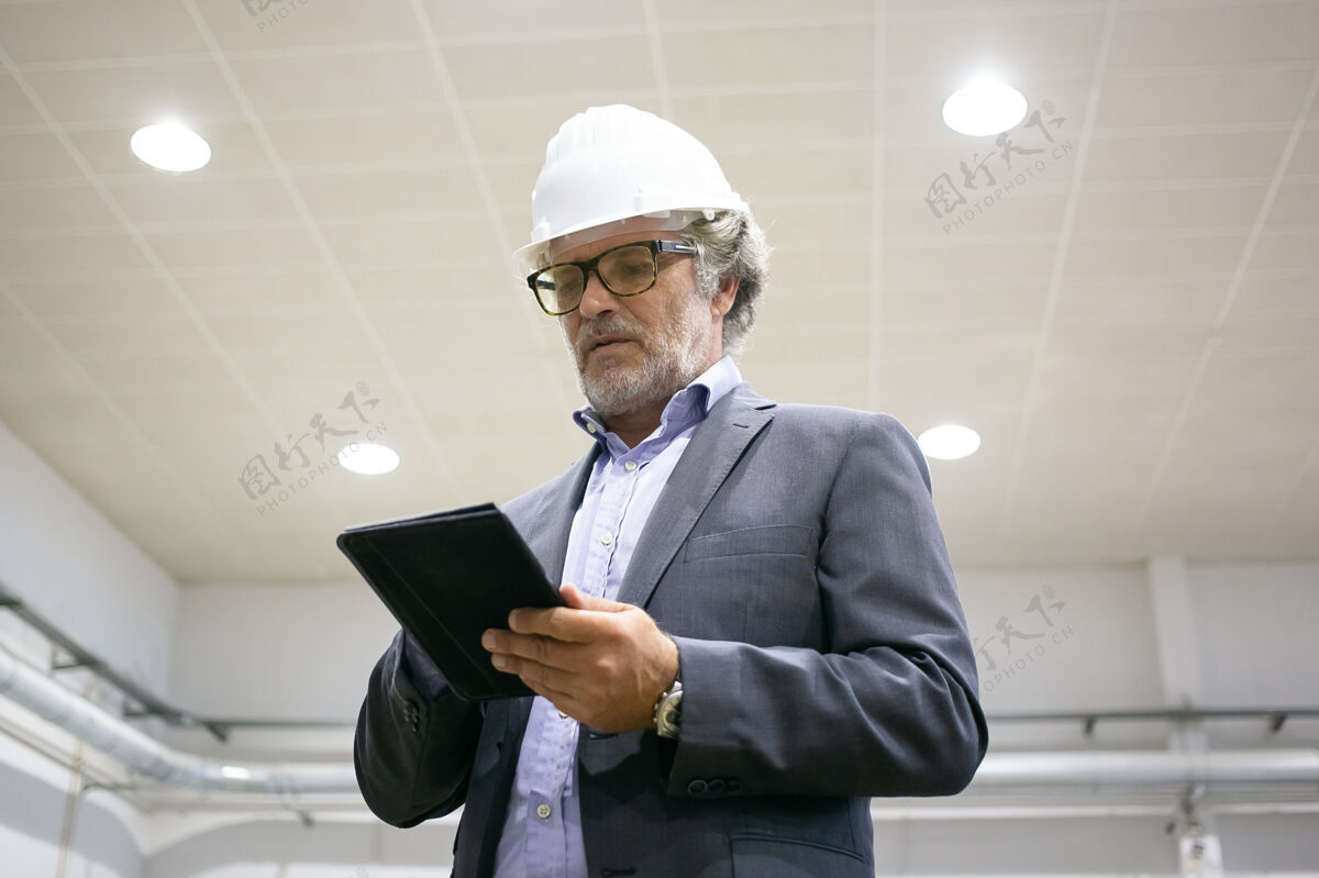 经验丰富体贴的男人戴着防护头盔拿着平板电脑看着屏幕人工作平板电脑