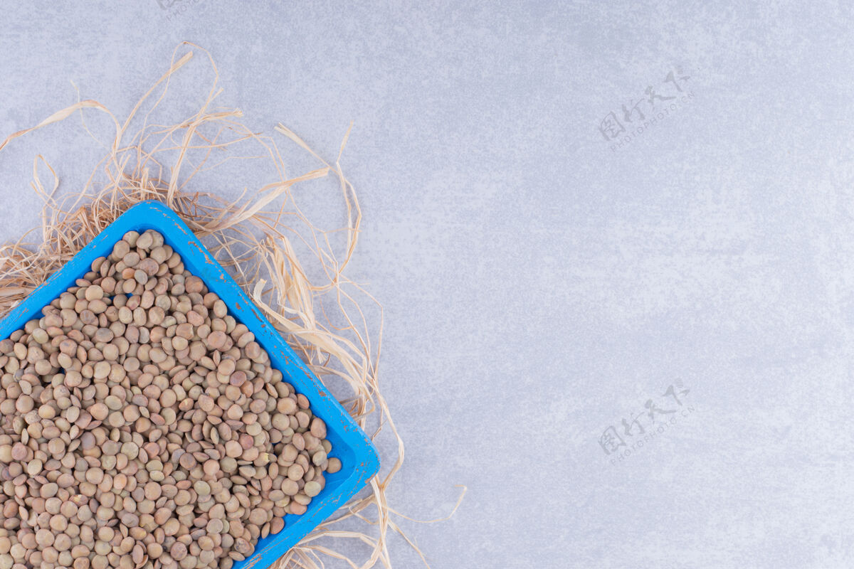 托盘一堆稻草上的蓝色托盘 大理石表面堆满了棕色小扁豆营养扁豆农业