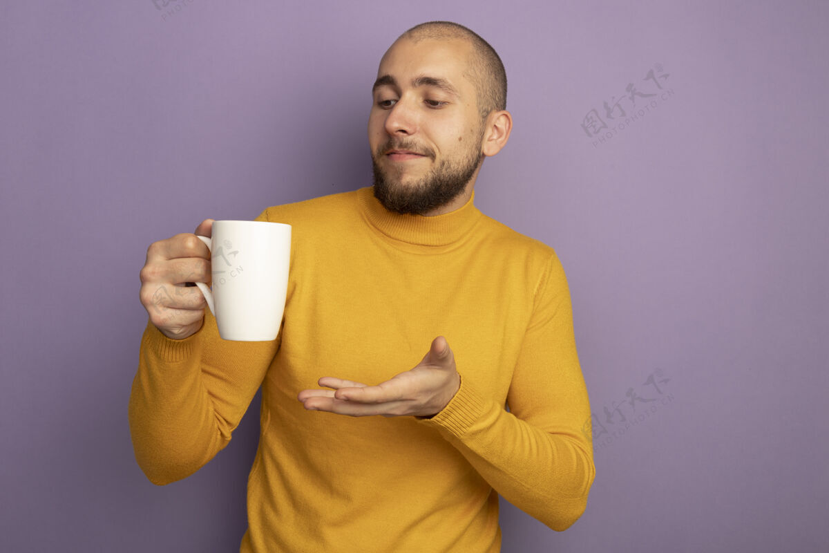 帅哥高兴的年轻帅哥捧着一杯茶 用手指着隔离在紫色墙壁上的临摹空间茶手拜托