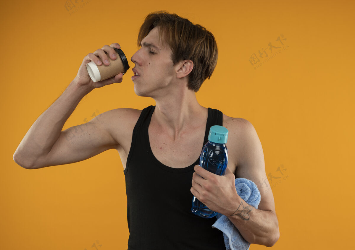 请喜欢闭上眼睛的年轻运动型男人拿着毛巾和水瓶 喝着橘色墙上的咖啡拿着的男的封闭的