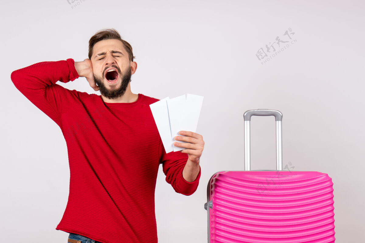 情绪正面图年轻男子手持粉色包和机票上白墙航班彩色旅游度假照片感慨成人颜色机票