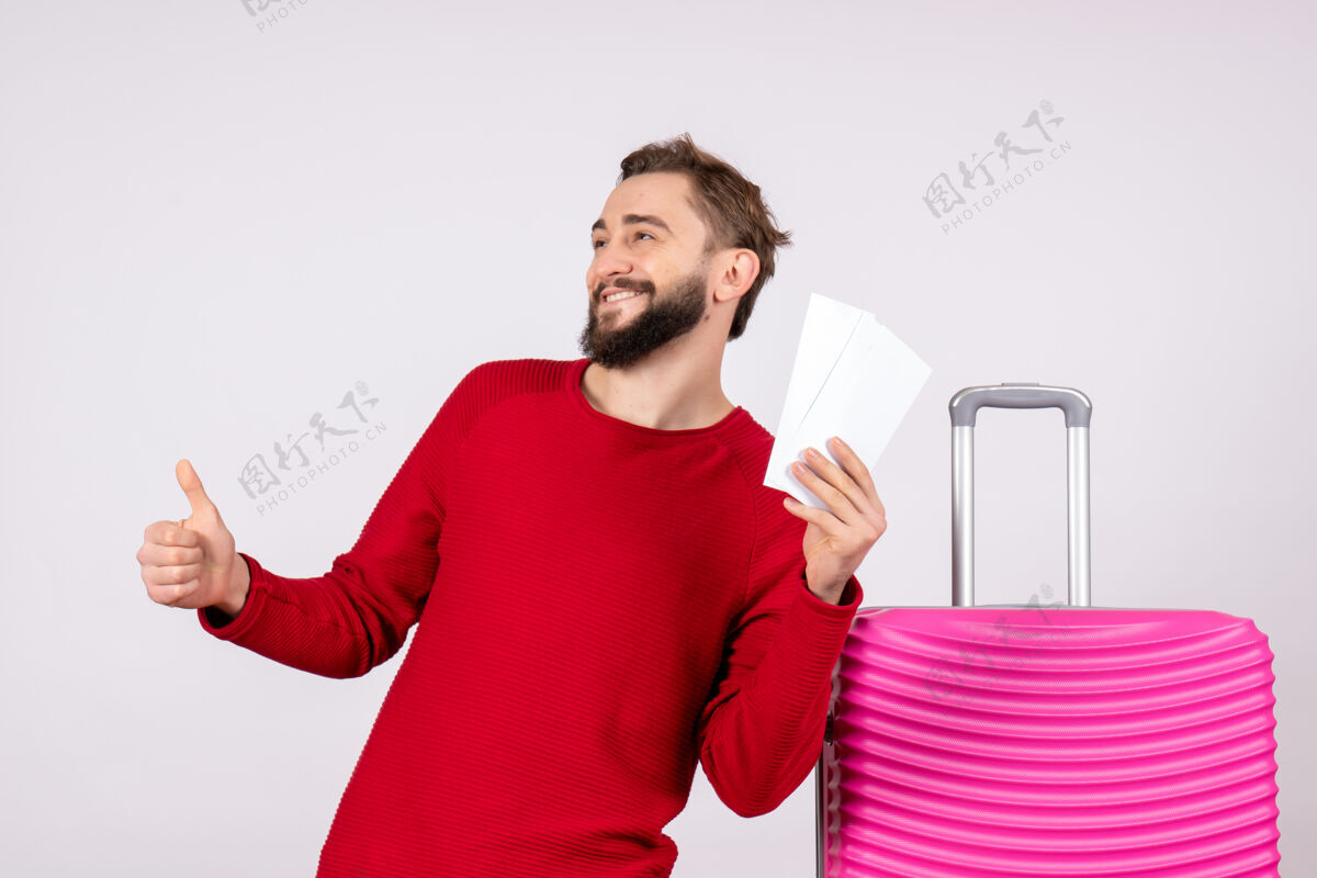航班正面图：年轻男子手拿粉色包 手持飞机票在白墙上航行飞行旅游度假情感照度假情感肖像