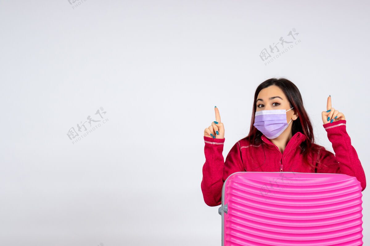女人正面图：年轻女性带着粉色袋子在白色墙壁上戴着无菌口罩旅行彩色假期柯维德女性病毒大流行风景年轻女性游客