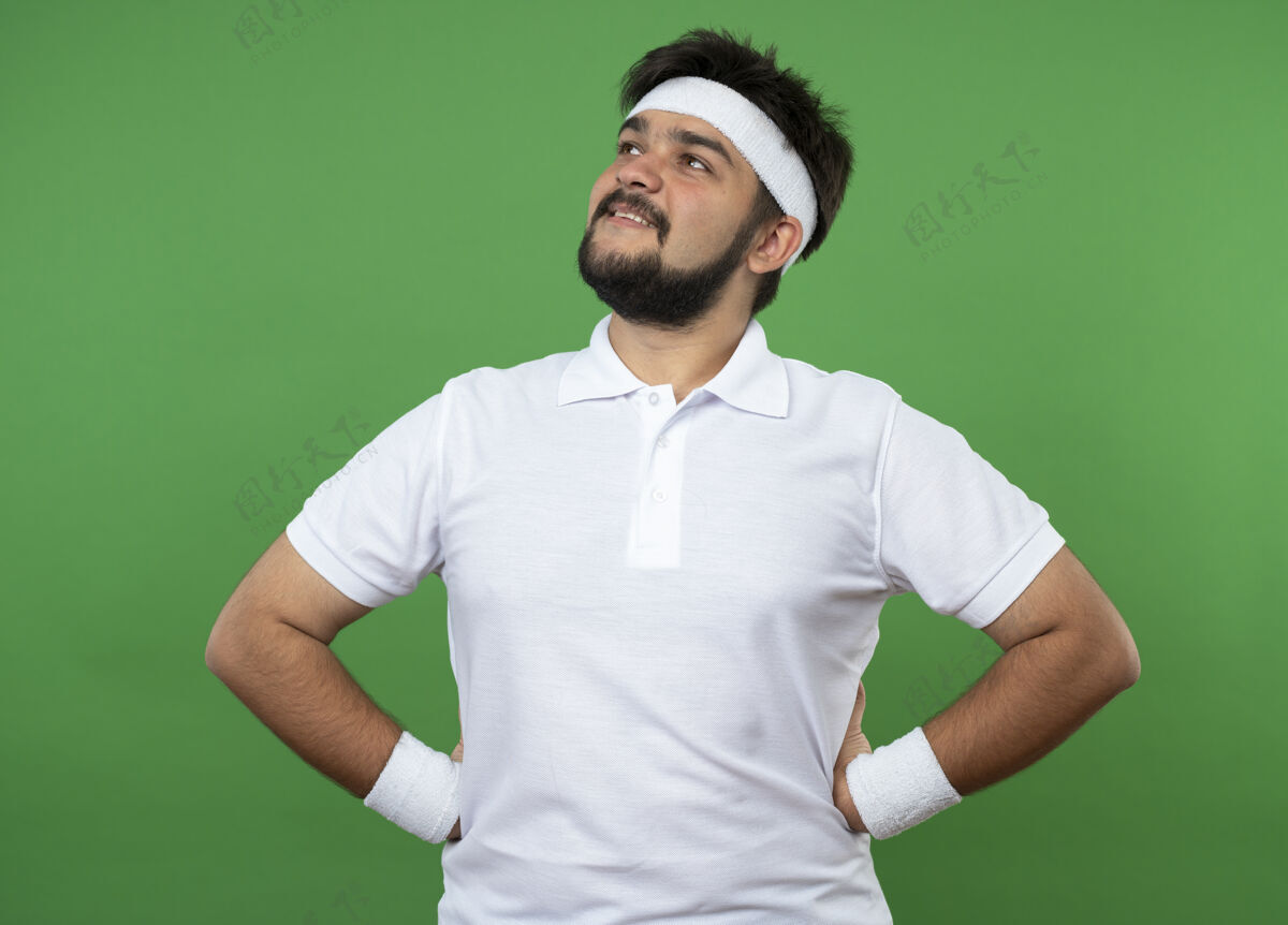 臀部高兴的年轻运动男子一边看着戴着头带和腕带把手放在臀部隔离在绿色头带腕带请穿