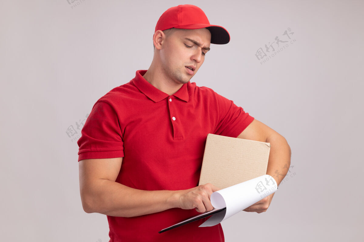 制服想着年轻的送货员穿着制服 拿着帽子盒 看着他手上的剪贴板孤立在白墙上年轻思考剪贴板